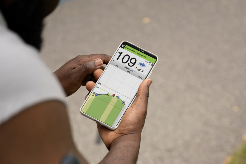 A person holds a smartphone displaying a glucose monitoring app with a reading of 109 mg/dL.